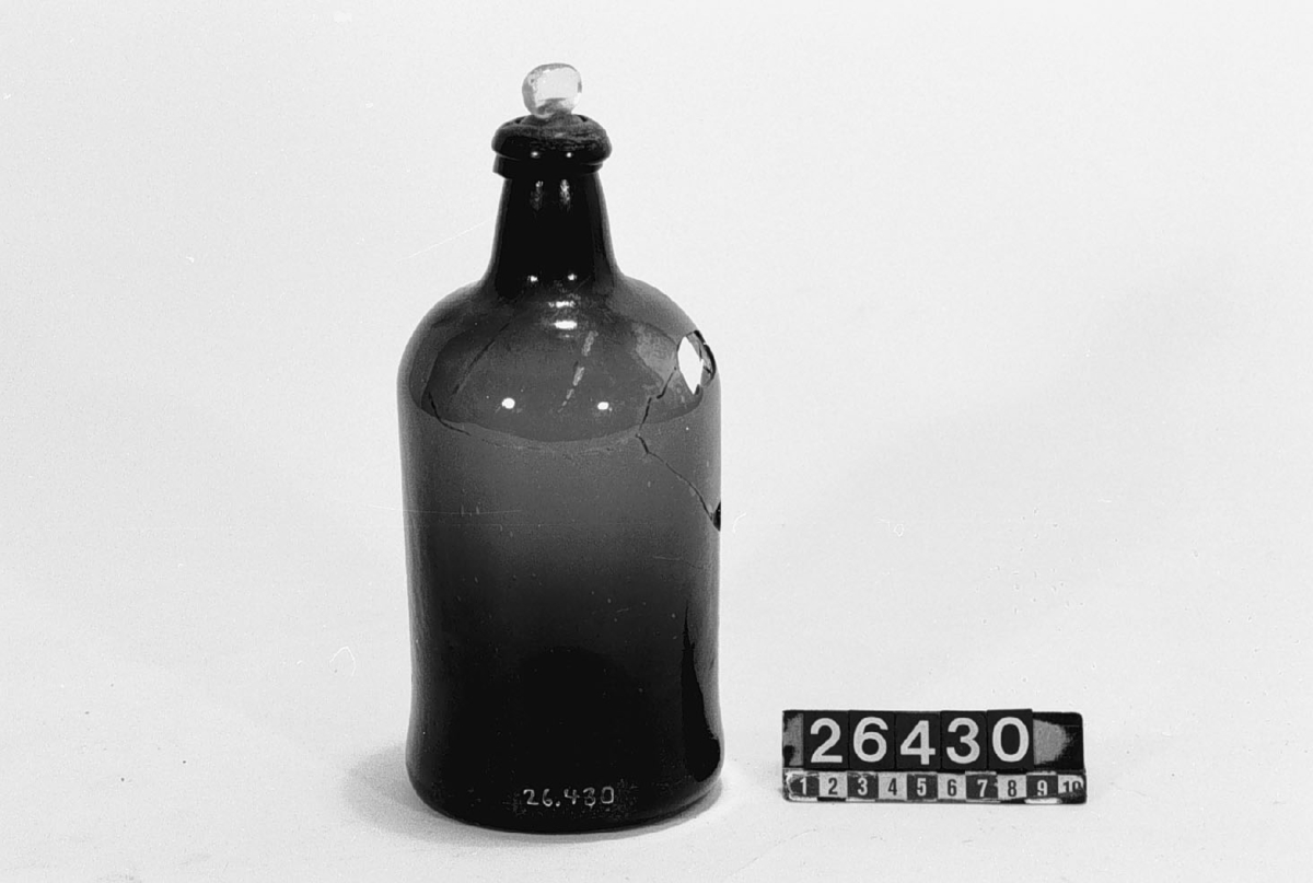 Butelj av grönt, blåsigt glas med inslipad propp, volym ca 1.15 liter. Etsat på halsen: "1 15 1/4".