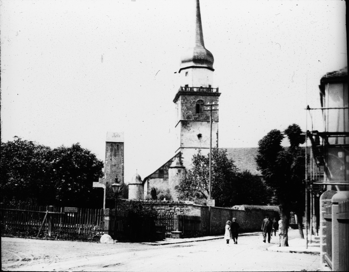 Skioptikonbild med motiv av Stadtpfarrkirche Sankt Kilian, Fladungen, vid sidan ett torn i stadsmuren.
Bilden har förvarats i kartong märkt: Vårresan 1910. Fladungen 7. X.