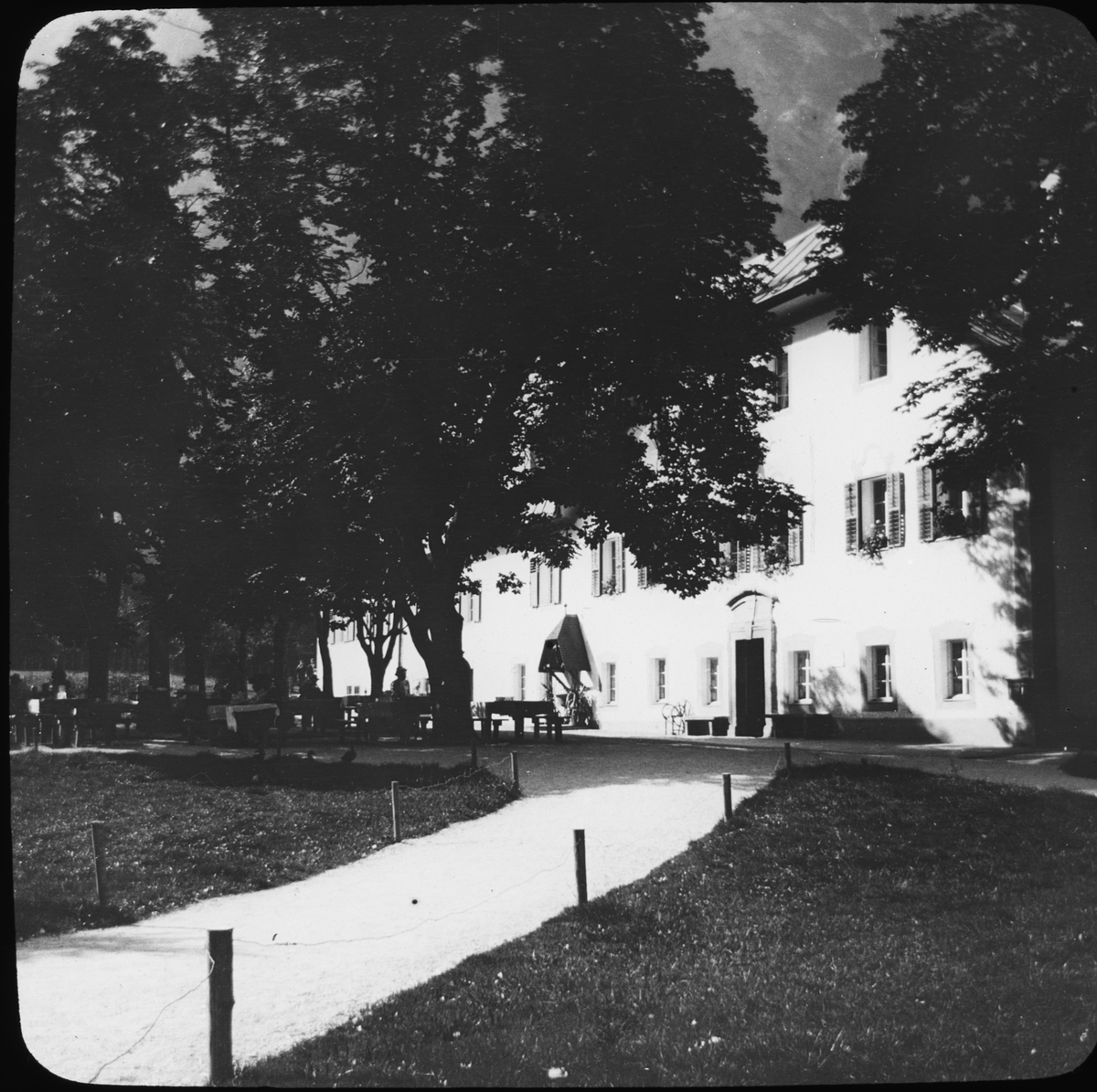 Skioptikonbild med motiv av byggnad, möjligen i Bartholomä.
Bilden har förvarats i kartong märkt: Höstresan 1910. Alhambra 9. N:22. Text på bild: "Der Köningssee".