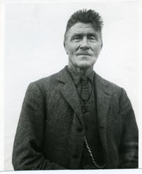 Portrett av en mann iført slips og dress. Mannen har bart og