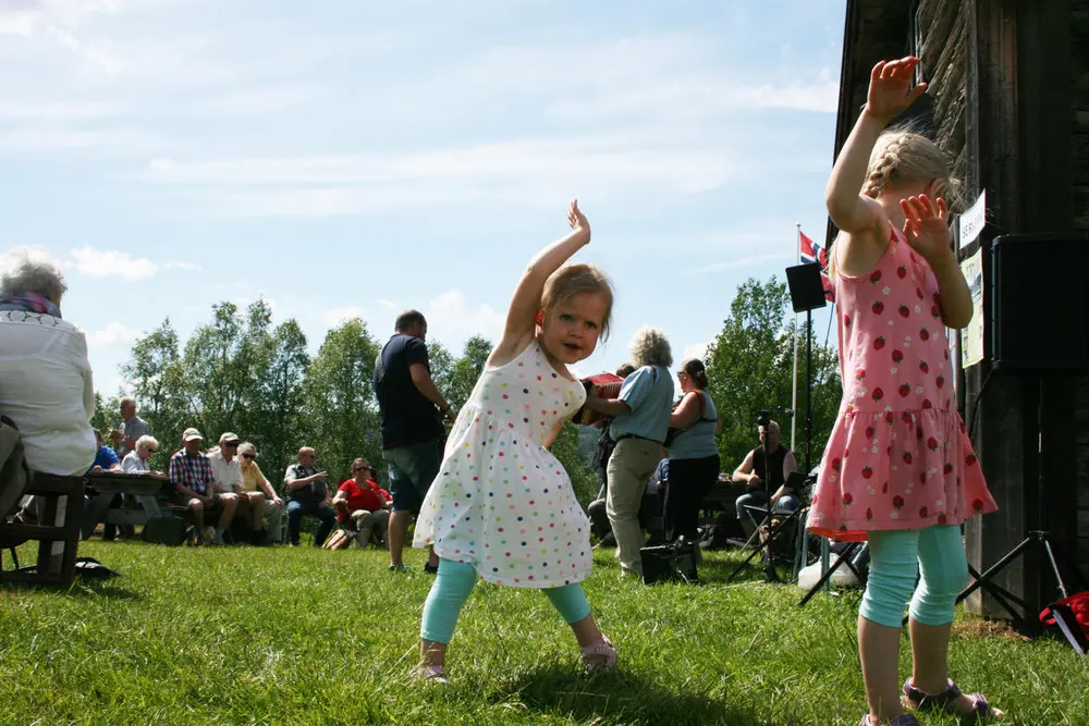 Sommerstemninga på tunet. To jenter danser og leker til musikk som spilles. De som spiller står i bakgrunnen og det er et publikum som hører på.