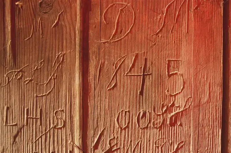 Diverse inskripsjoner gravert inn i treverk. Man kan blant annet se bokstavene "L, H, S" og tallet "1845".