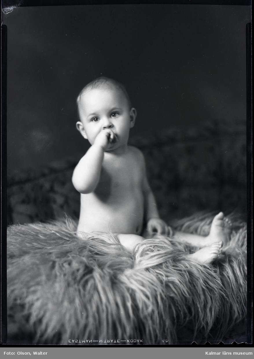 Ateljéfoto. Baby sittande på fårskinnsfäll.