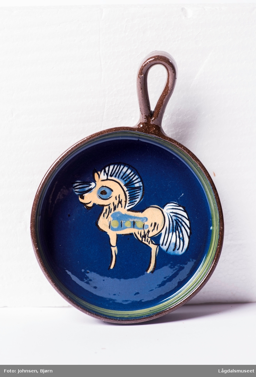 Liten panne med hank. Pannen er dekorert med et motiv av en gul hest på blå bakgrunn.