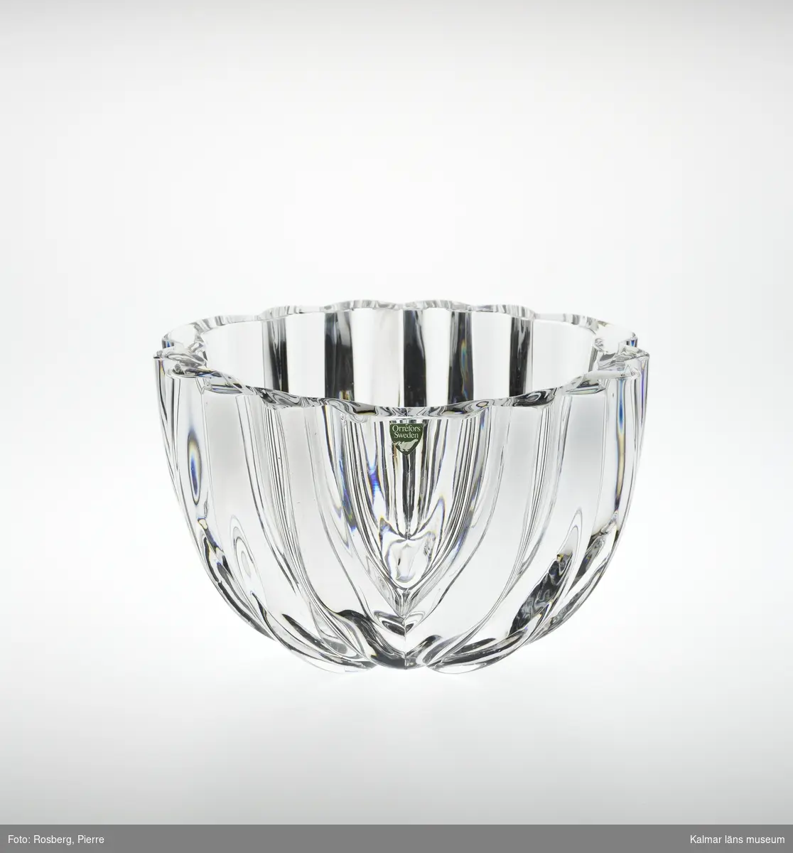 KLM 45619:193. Skål. Av ofärgat kristallglas. Rund form med veckad utsida, formad som ett stort blad. Upptill en klisterlapp: Orrefors Sweden.