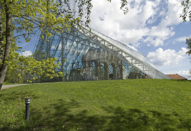 The catedral ruins covered by the protective construction in glass and steel surrounded by trees, lawn and summer sky.