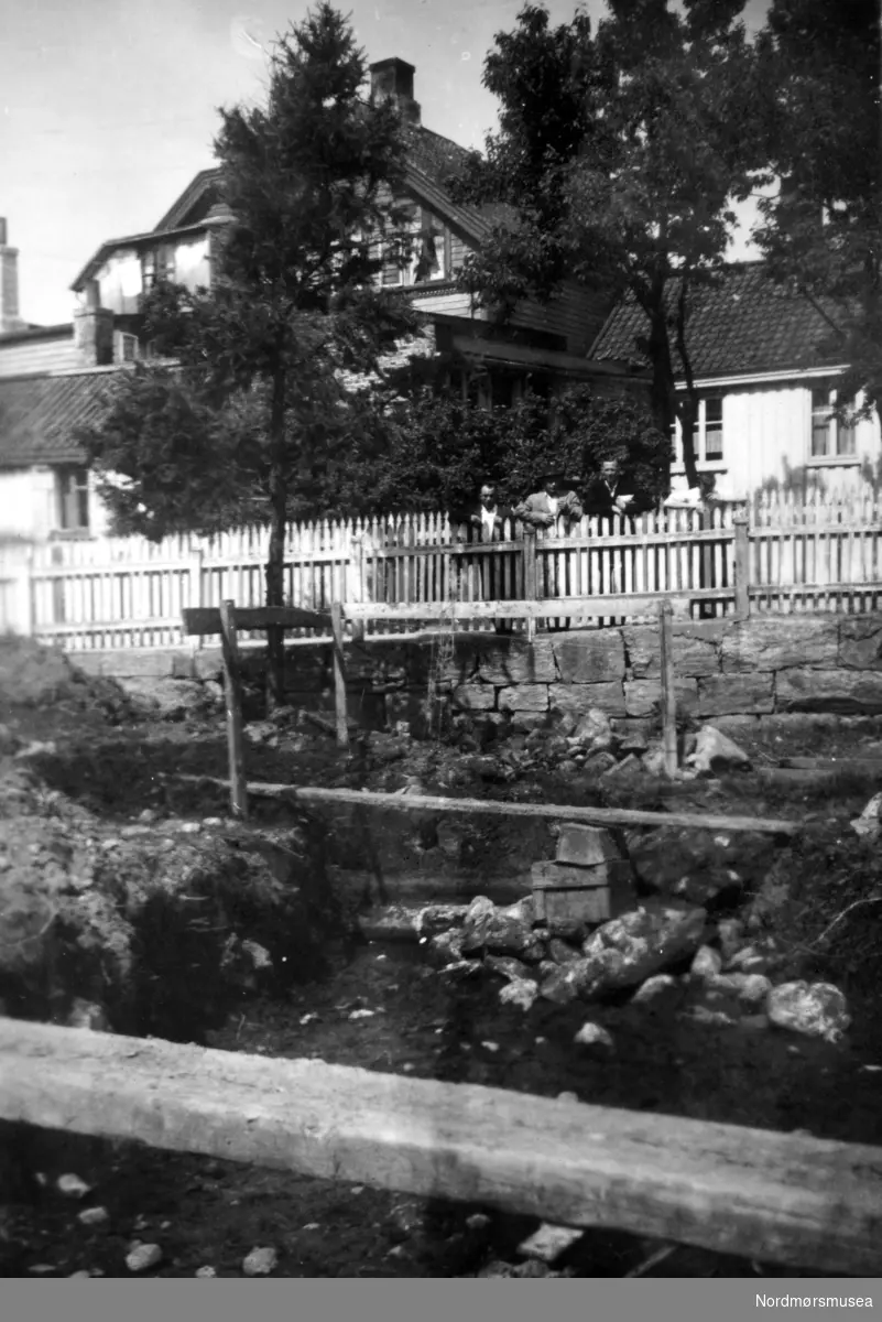 På bildet ser vi pågående gravearbeid på en tomt sør for Knudtzongården på Innlandet, revet 1979. Der ble det funnet - til venstre på bildet - en av de gamle brønnene tilhørende denne Knudtzongården. I bakgrunnen ser vi Loennechengården og Rødalgården med flere, som er gårder mellom Knudtzongården og denne tomten. Se Yderstads notater, bind 7 side 142. Se også 1947/899 (KMb-1947-000.0899.jpg) Bildet er datert Juni 1947. Fra Nordmøre Museums fotosamlinger.