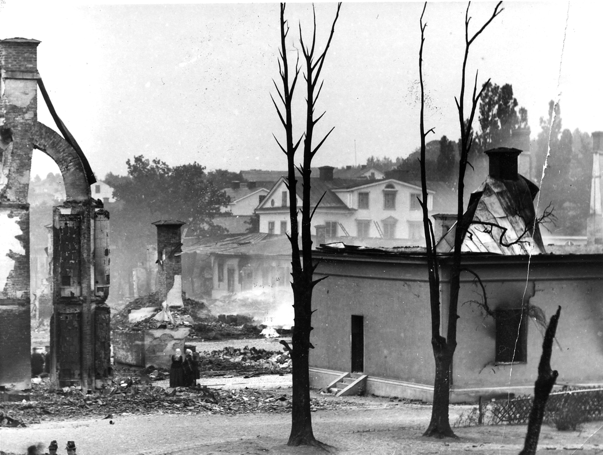 Fotografi efter Köpingsbranden 1889, av C. Billberg. Till vänster är endast skorstensstockarna kvar efter den nedbrunna Havreettan Erikssons gård, Till höger det som återstår av Mälarbanken. Bakom denna ser man Basargården på håll.