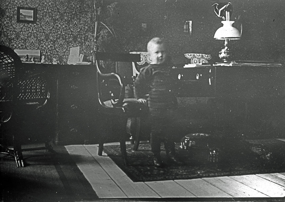 Ett barn bredvid en stol och ett bord. Fotograf Alfred Bergendahl. Givare H Bergendahl.