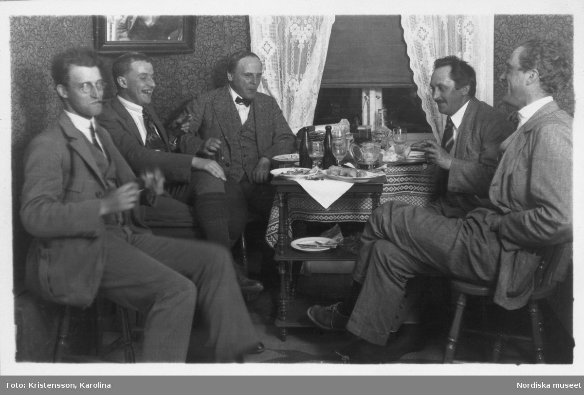 Fem män sitter runt ett bord på Älvdalens gästgivaregård och äter en måltid. från vänster fotograf Olle Ekberg, fil. dr. Bertel Hintze, intendent Sigurd Erixon (expeditionens ledare), antikvarien Ola Bannbers och arkitekt Mogens Mogensen. Bilden är tagen under Sigurd Erixons expedition i Ovansiljan 1926.