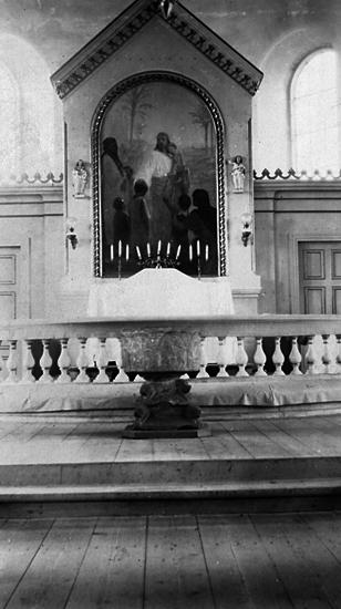 Foto i kyrkan mot altarrundeln. Framför står en dopfunt.