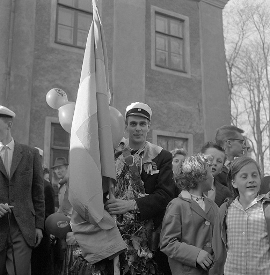 Studenterna, tredje d. 1960. 
En fanbärare m.fl. vid Esaias Tegnérs staty.  I bakgrunden syns det
s.k. Karolinerhuset.