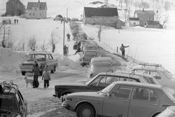 Parkerte biler og skiløpere i Sørlia. Bebyggelse i bakgrunne