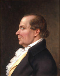 Portrett av Peder J. Cloumann. Profil. Mørk drakt, hvit skjorte med kalvekryss, lys gul vest.. Foto/Photo