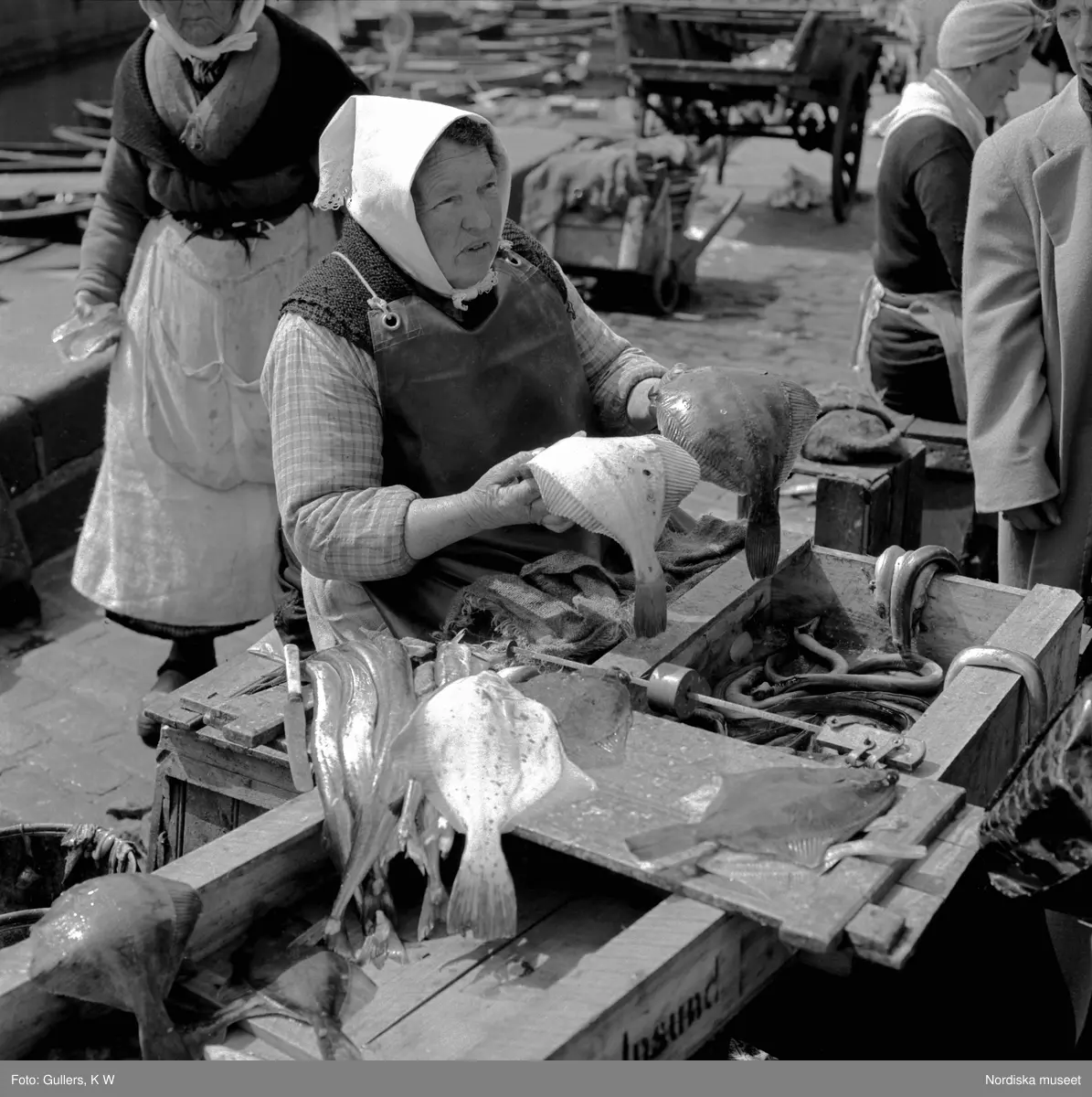 Torghandel, Stockholm. Äldre kvinna med huckle på huvudet säljer fisk.