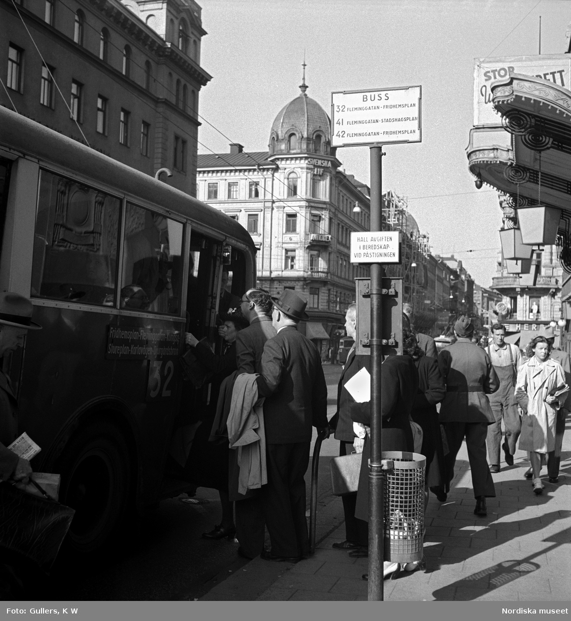 Passagerare köar till buss nummer 32 vid en hållplats utanför Oscarsteatern på Kungsgatan, Stockholm.