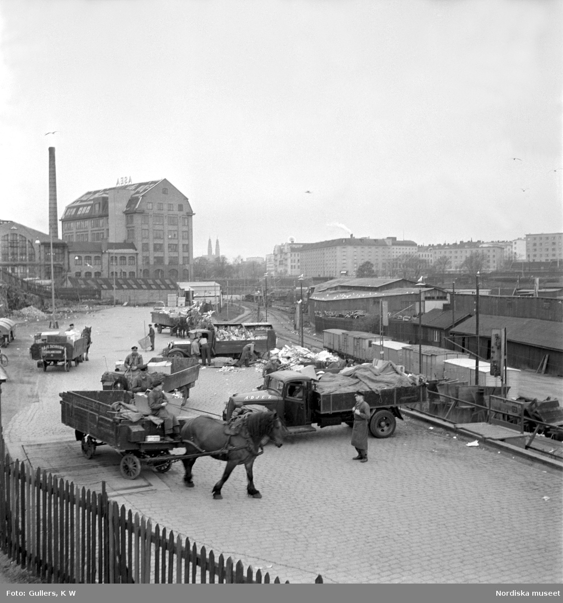 Södermalm, Stockholm. Sopåkare vid Södra stationsområdet tömmer sina kärror i den väntande godsvagnarna. Lossning, lastbilar och hästar med kärror. Järnvägsspår.