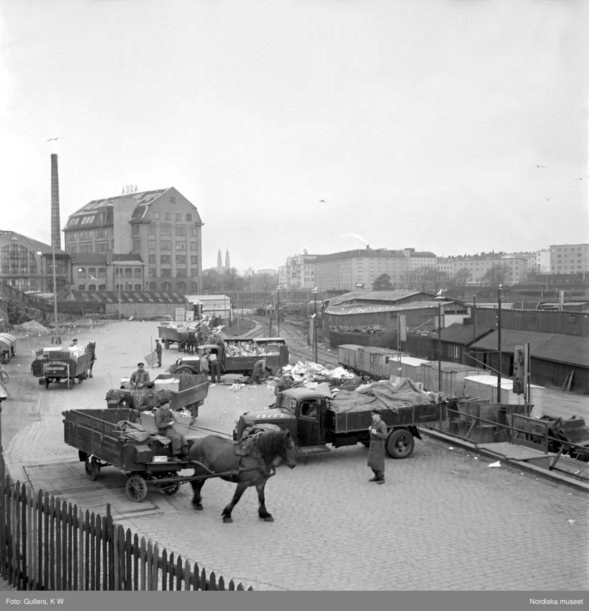 Södermalm, Stockholm. Sopåkare vid Södra stationsområdet tömmer sina kärror i den väntande godsvagnarna. Lossning, lastbilar och hästar med kärror. Järnvägsspår.