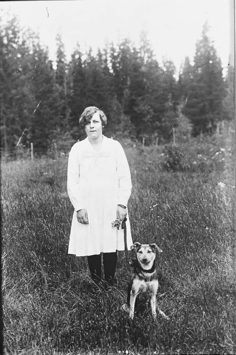 Anna Løvlibråten stående med hund ute i en eng.