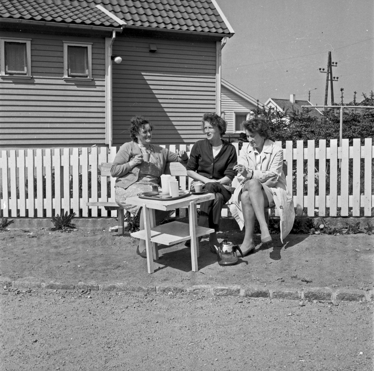 Kaffepause. Tre kvinner på en benk nyter solen og en kaffetår.
