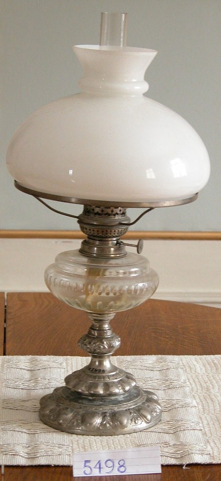 Lampa, fotogen-. Det är en bordslampa med vit kupa och fot av förnicklad mässing.