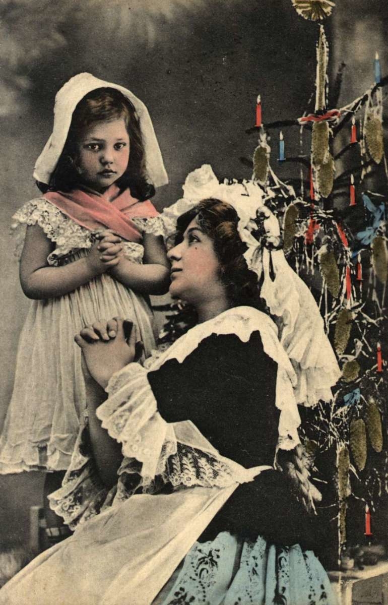 Julekort. Nyttårshilsen. Kolorert fotografi. Kvinne og pike i bønn ved juletreet. Stemplet antatt 1908.