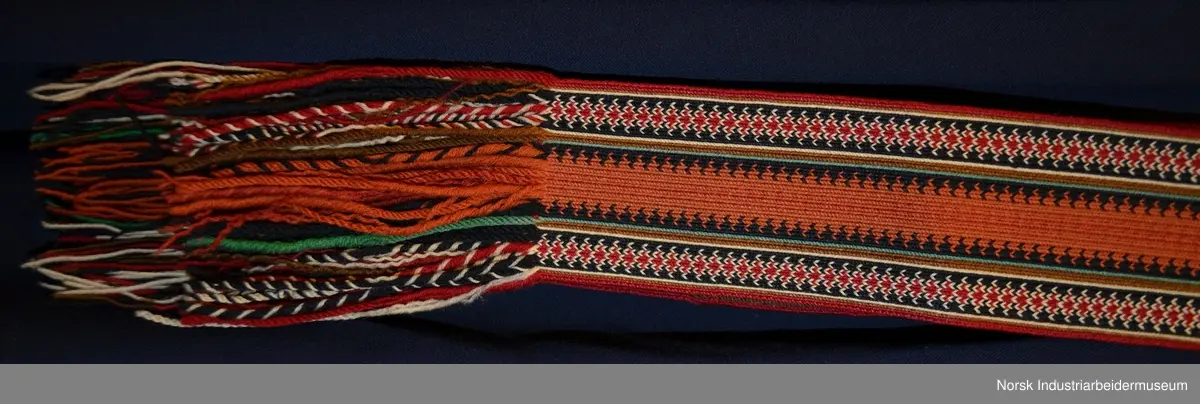 Livet er foret med et ubleket stoff. Livet er mørkt blått med grønn kanting. Både kantene og livet er prydet med plattsøm foran og bak. 
Nederst på stakken er det to border. Den øverste er  i grønt kantet med lilla og orange kontursting. Den nederste er i rødt kantet med gult. Nedenfor bordene ses den mørkeblå stakken. Den er kantet med rødt. 
Det brikkevevde beltet som hører til bunaden er sydd fast i kanten på livet. Borden i midten er orange og svart. På hver ytterside er det en rød, hvit og svart bord. Beltet har også striper i brunt, hvitt, rødt, svart og turkis. Beltet lukkes med hekter. Begge frynseendene på beltet er klipt av. Det ene frynesstykket er montert på beltet, slik at det alltid henger ned langs stakken i samme lengde. Det andre frynsestykket er løst og må festet på beltet med en sikkerhetsnæl eller liknende.