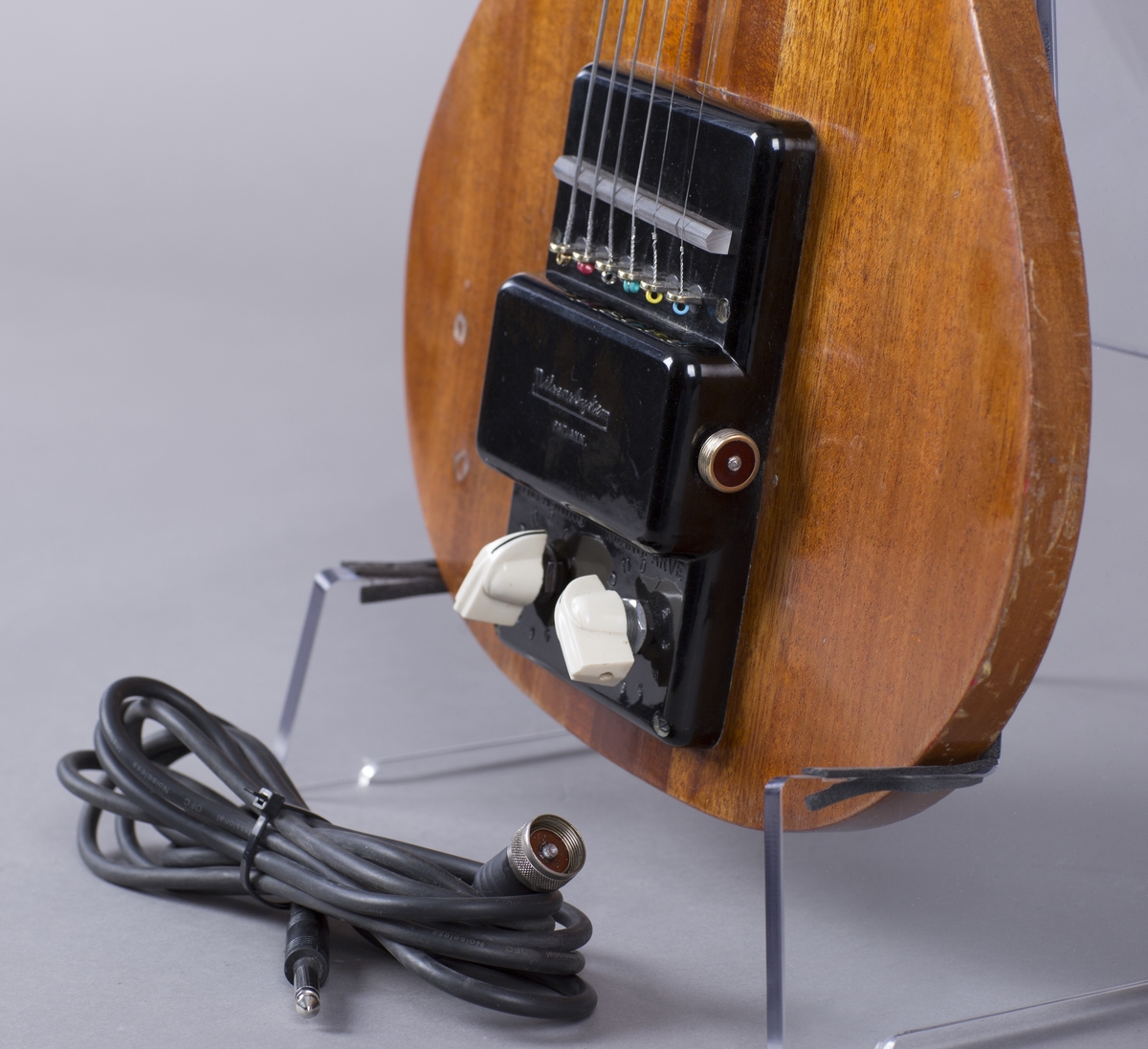 Elektrisk gitar med kropp og hals av mahogny. Magnet ved halsfeste og pickup ved strengefeste (NilsensSystem). Kontrollere for tilpasning og klangfarge. Tilpasning tilsvarer volum og gir størst volum på nivå 1. Enkelte av stemmeskruene er ikke originale.