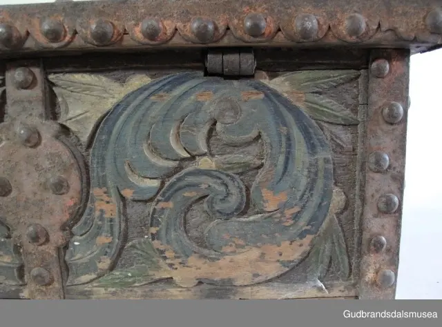 "Bladformer, smøygde band og drageornamentikk. Millom kantjarn og utskurden hev lokket fint utskorne små blad og halvrunde aggar. Vel vedlikehalde, sterk jarning og prydelege gangjarn. Truleg frå 1500 talet. Fra Haugen, Øystre Gausdal". (Jf. "Katalog for Lom Bygdesamling,1925).
Skrinrammen er holdt sammen av utvendige hjørnekantbeslag; jernhandtak i hver side. Fronten har nøkkelhullslås med beslag rundt. Lokket er satt samen av 2 bord, forsterket med jernbeslag rundt kanter på overside; to hengselbeslag festet til innside av lokk og bakstykke. Skrinsider blir holdt sammen av beslag ned langs hjørnekanter; har jernhandtak festet på jernbeslag.
Bunnen er satt sammen av 2 bord, festet til hverandre med to forsenka treplugger; bunnen var opprinnelig festet til underkant av skrinsider med 4 x 4 trenagler,seinere festet med spiker. 
Det er jernbeslag  på bakstykket midt, rundt hjørnekanter, omkring nøkkelhullslås, rundt lokk samt 2 handtak med beslag. Alle beslag er festet med store jernnagler; beslag på sidestykker er festet med små jernnagler under skrinbunnen. 3 av 8 bunnfester for beslag er fortsatt intakte.
DEKOR. De store jernnaglene med forskjøvet plassering på beslag ble sannsynligvis brukt som dekorelement; runde beslag på sider, bakstykke og front. Flatskurd på lokk med flettet, stilisert renessanseranke, der bladverk er "omgjort" til småspiraler eller rundinger.  På skrinsidene akantusskurd med c-former, bladtunger uten stilk og naturalistiske småblad i rokokkostil. Flatskurd var vanlig i Gudbrandsdalen i perioden ca. 1650-1750, mens akantusmotivet først ble vanlig på bruksgjenstander i løpet av siste halvdel av 1700-tallet. Den mørkere grønne og blå dekorfargen var vanlig i siste del på 1700-tallet; den brune bunnfargen var vanlig i bruk fra 1780-tallet. 
BRUK. Før kofferten kom i bruk hadde man reiseskrinet, som ble brukt til oppbevaring av bl.a. klær, verdisaker og mat på reiser. Skrinet hadde ofte et eller to mindre, smale rom langs den ene skrinsiden og ett større rom. De fleste reiseskrin var i tillegg forsterket med jernbeslag langs alle kanter og med en solid nøkkelhullås til sikring mot støt, slag og tyveri.