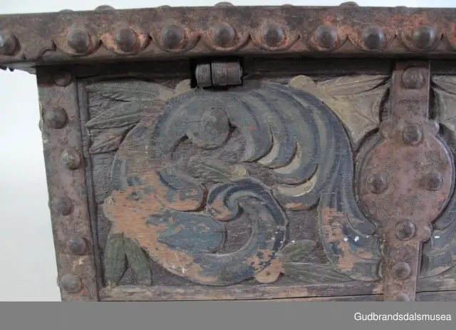 "Bladformer, smøygde band og drageornamentikk. Millom kantjarn og utskurden hev lokket fint utskorne små blad og halvrunde aggar. Vel vedlikehalde, sterk jarning og prydelege gangjarn. Truleg frå 1500 talet. Fra Haugen, Øystre Gausdal". (Jf. "Katalog for Lom Bygdesamling,1925).
Skrinrammen er holdt sammen av utvendige hjørnekantbeslag; jernhandtak i hver side. Fronten har nøkkelhullslås med beslag rundt. Lokket er satt samen av 2 bord, forsterket med jernbeslag rundt kanter på overside; to hengselbeslag festet til innside av lokk og bakstykke. Skrinsider blir holdt sammen av beslag ned langs hjørnekanter; har jernhandtak festet på jernbeslag.
Bunnen er satt sammen av 2 bord, festet til hverandre med to forsenka treplugger; bunnen var opprinnelig festet til underkant av skrinsider med 4 x 4 trenagler,seinere festet med spiker. 
Det er jernbeslag  på bakstykket midt, rundt hjørnekanter, omkring nøkkelhullslås, rundt lokk samt 2 handtak med beslag. Alle beslag er festet med store jernnagler; beslag på sidestykker er festet med små jernnagler under skrinbunnen. 3 av 8 bunnfester for beslag er fortsatt intakte.
DEKOR. De store jernnaglene med forskjøvet plassering på beslag ble sannsynligvis brukt som dekorelement; runde beslag på sider, bakstykke og front. Flatskurd på lokk med flettet, stilisert renessanseranke, der bladverk er "omgjort" til småspiraler eller rundinger.  På skrinsidene akantusskurd med c-former, bladtunger uten stilk og naturalistiske småblad i rokokkostil. Flatskurd var vanlig i Gudbrandsdalen i perioden ca. 1650-1750, mens akantusmotivet først ble vanlig på bruksgjenstander i løpet av siste halvdel av 1700-tallet. Den mørkere grønne og blå dekorfargen var vanlig i siste del på 1700-tallet; den brune bunnfargen var vanlig i bruk fra 1780-tallet. 
BRUK. Før kofferten kom i bruk hadde man reiseskrinet, som ble brukt til oppbevaring av bl.a. klær, verdisaker og mat på reiser. Skrinet hadde ofte et eller to mindre, smale rom langs den ene skrinsiden og ett større rom. De fleste reiseskrin var i tillegg forsterket med jernbeslag langs alle kanter og med en solid nøkkelhullås til sikring mot støt, slag og tyveri.