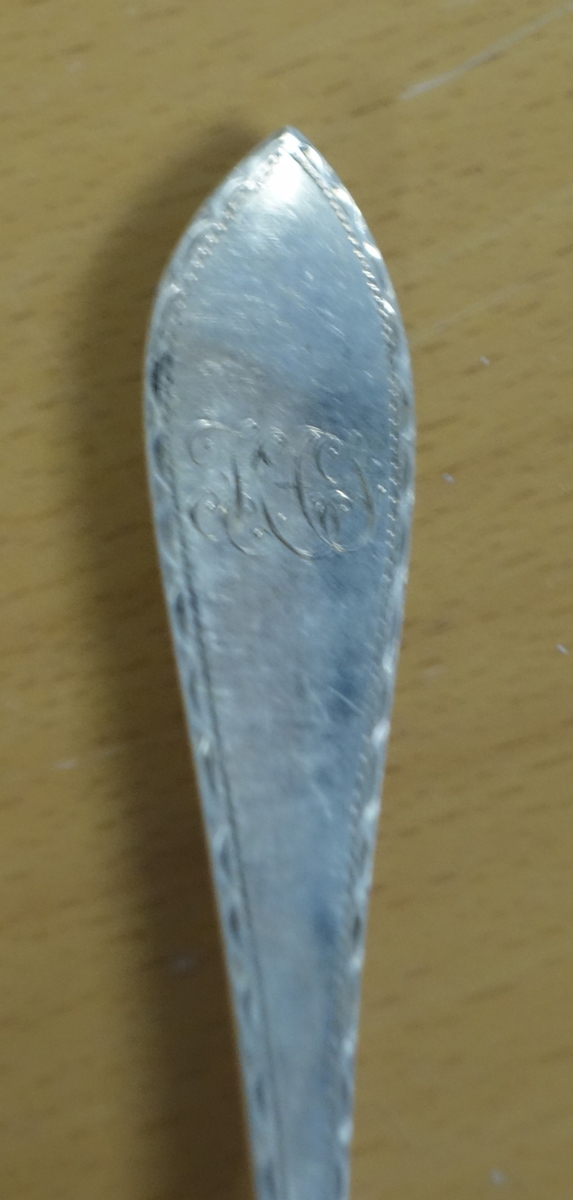 Spisegaffel av sølv av empiretype med  gravert kant. Gravert initialer på framsida av skaftet og dato på baksiden.