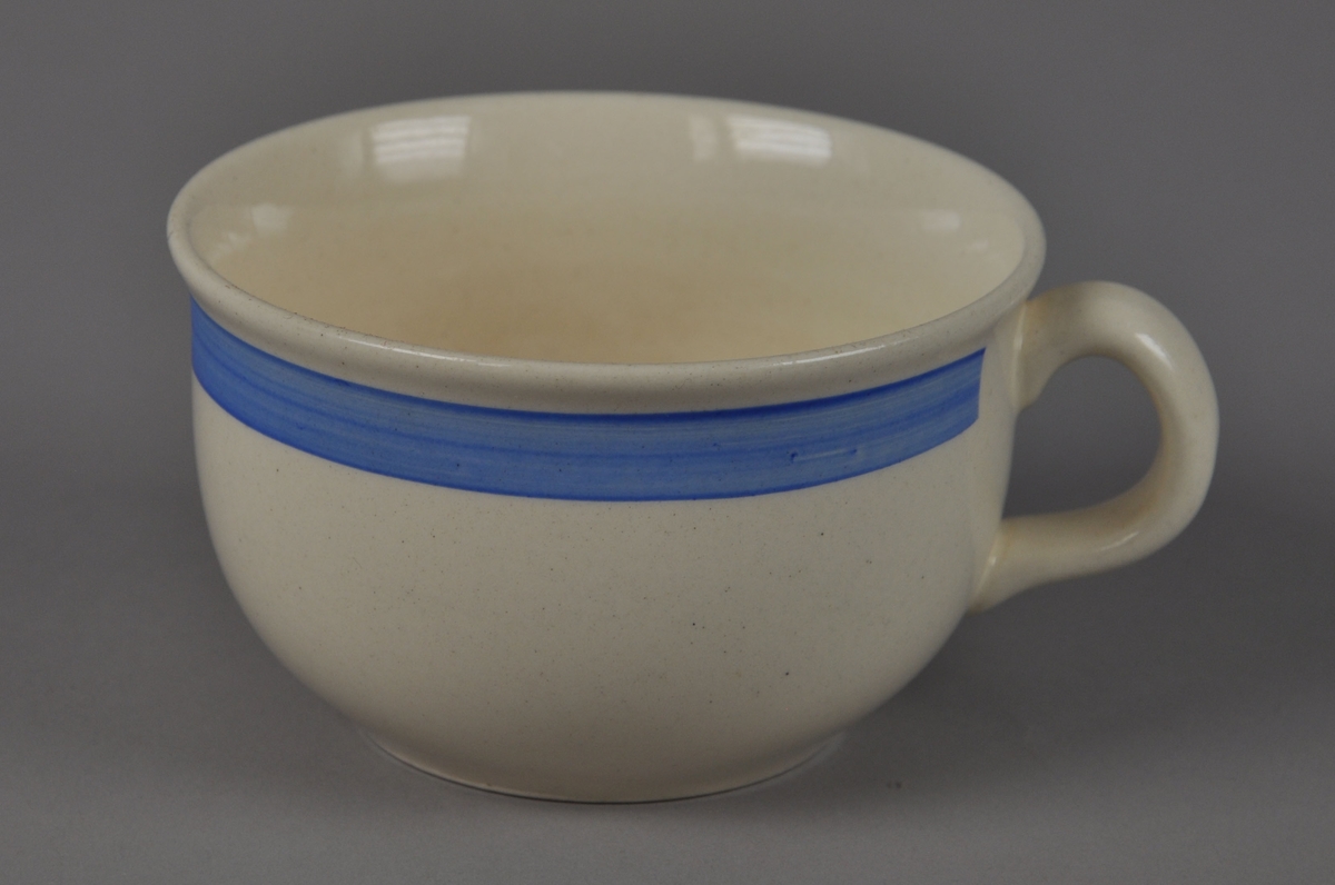 Kaffekopp av glassert keramikk, med hank. Koppen har en påmalt blå stripe rundt munningsranden.
