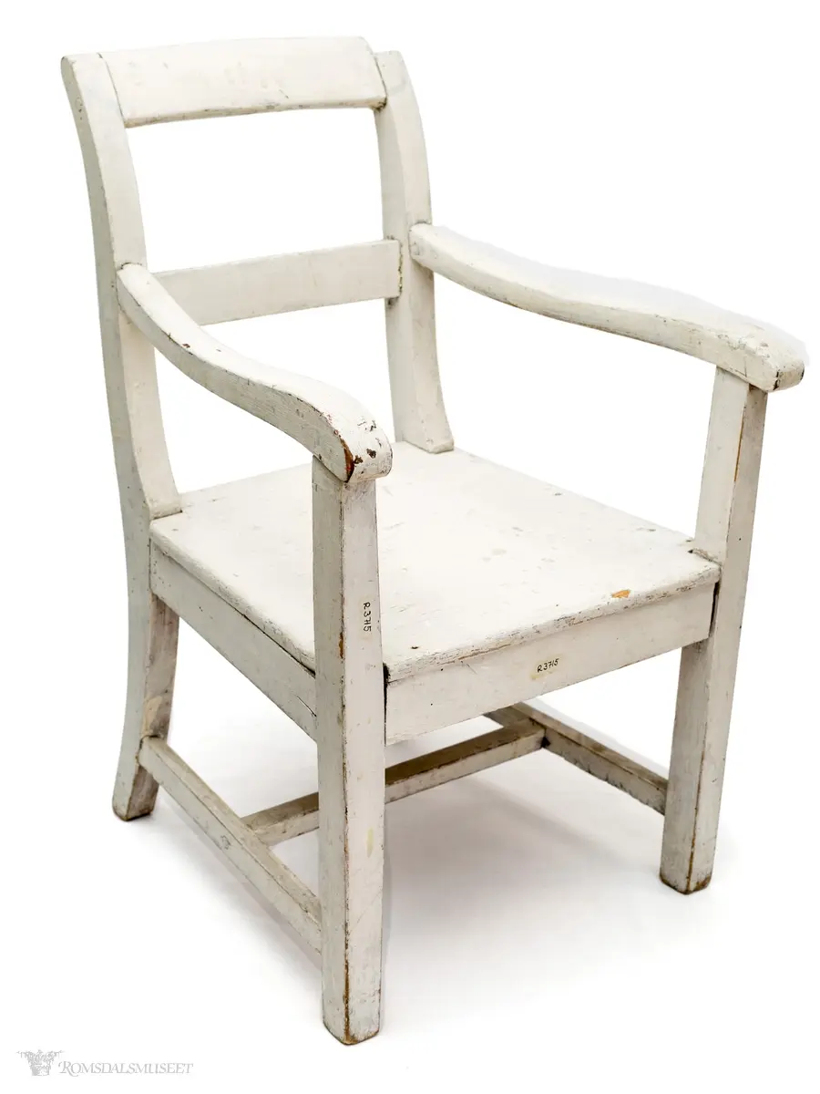 Hvitmalt barnestol i tre med rett fasong.  Stolen har 2 armlener og 1 tverrsprosse i ryggen.