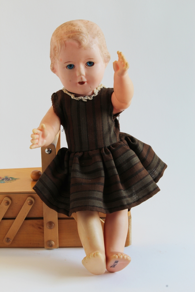 Gitt av Gerd Berit Lie. 
Dukken har knall blå øyne og røde lepper. Eier beskriver dukken som en "baby-dukke". Dukken ble vunnet på basar av moren til Gerd Berit, Elise, i ca 1960/61. Moren vant denne dukken samt en en annen dukke (KMR.3438).
