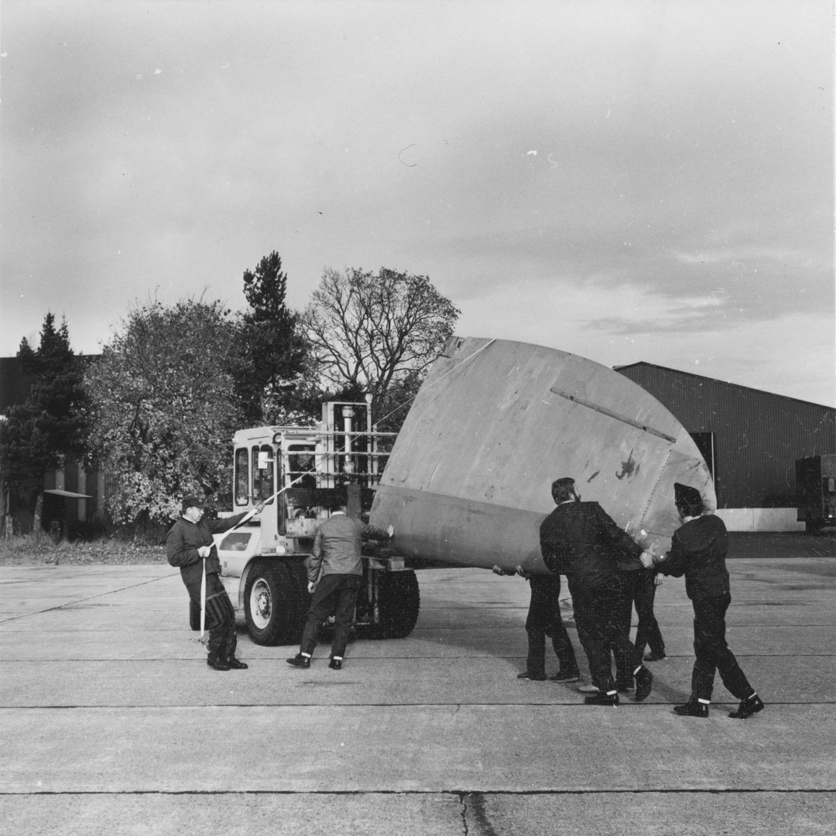 Flytt av vinge till flygplan Spitfire som anlänt till Flygvapenmuseum, på flygfältet på F 3 Malmen. Flygplanet har just anlänt från Kanada i transportflygplanet TP 84. Tekniker och flygvapenpersonal i arbete.