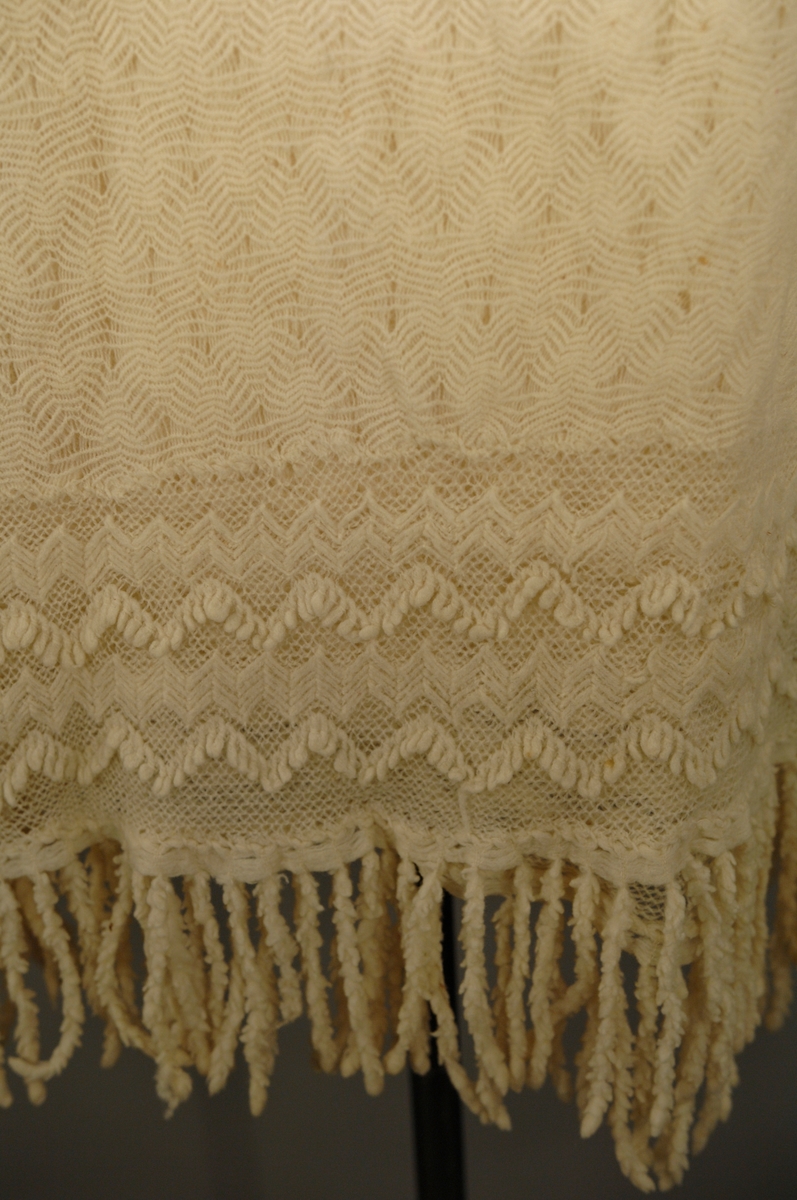 Strikket i tynn ulltråd. Den innerste firkanten er strikket i eit stykke. Knaten rundt påsydd slik at hjørnsne blir avrunda. Dersetter er det påsydd frynser med symaskin.