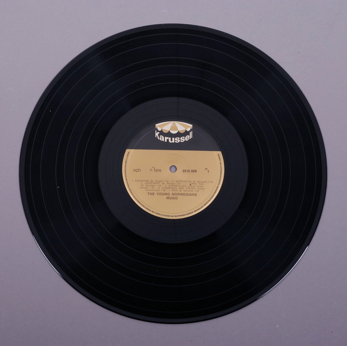 Grammofonplate i svart vinyl og plateomslag i papp. Plata ligger i en papirlomme som har bilder av andre utgivelser.