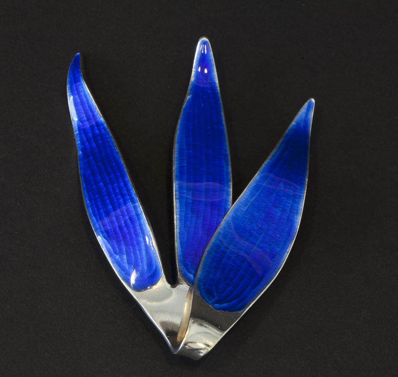 Brosje i sølv med blå speilemalje. Utformet som et tre blader