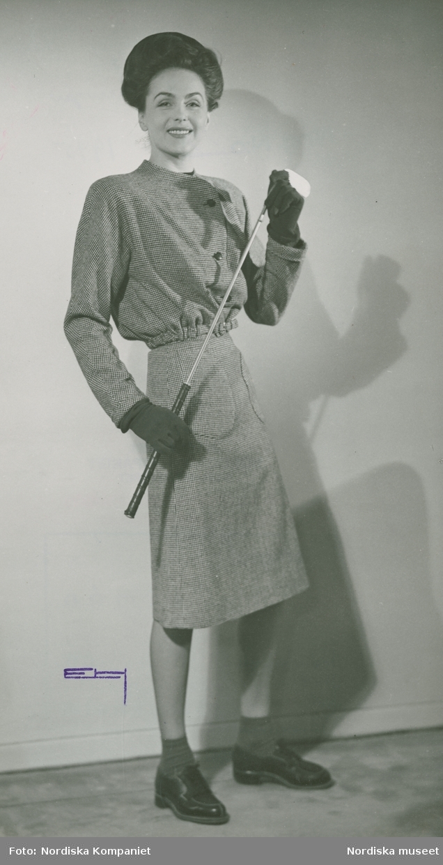 "Nytt och nyttig, kjolen är betydelsefull". Modellen o skådespelerskan Hjördis Genberg Niven  i kjol och jacka, handskar och snörskor, med golfklubba i handen. Från Grieder.