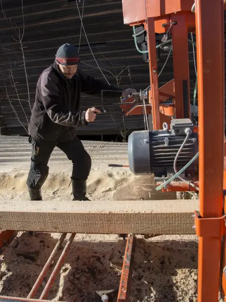 Tømrer starter opp ei stor, oransje sag som brukes til å sage plank.