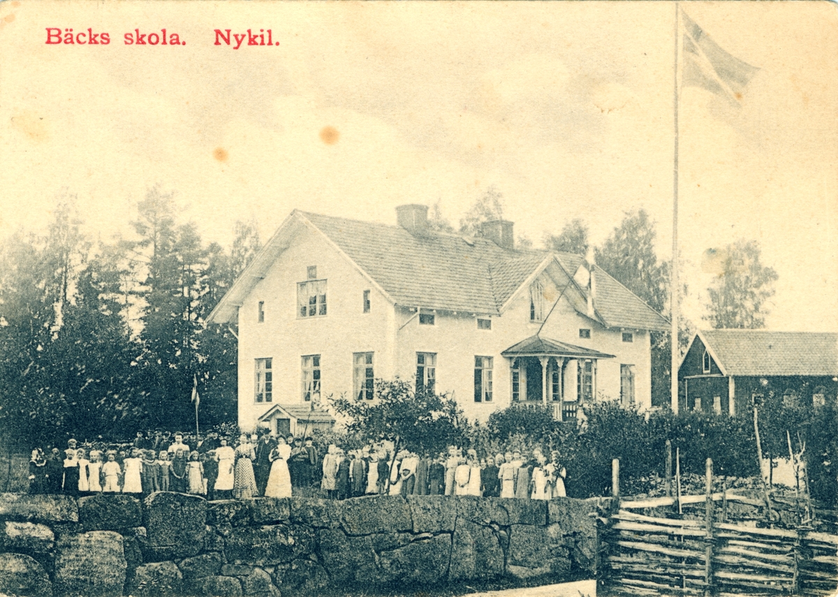 Orig. text: Bäcks skola. Nykil.
Skolan ligger på vägen mellan Wittsäter och Törnevik i Nykils socken. 1 km från Wittsäters-Korset på höger sida. Huset ser litet ut även idag och används som bostad. Föreställer troligen en skolavslutning.