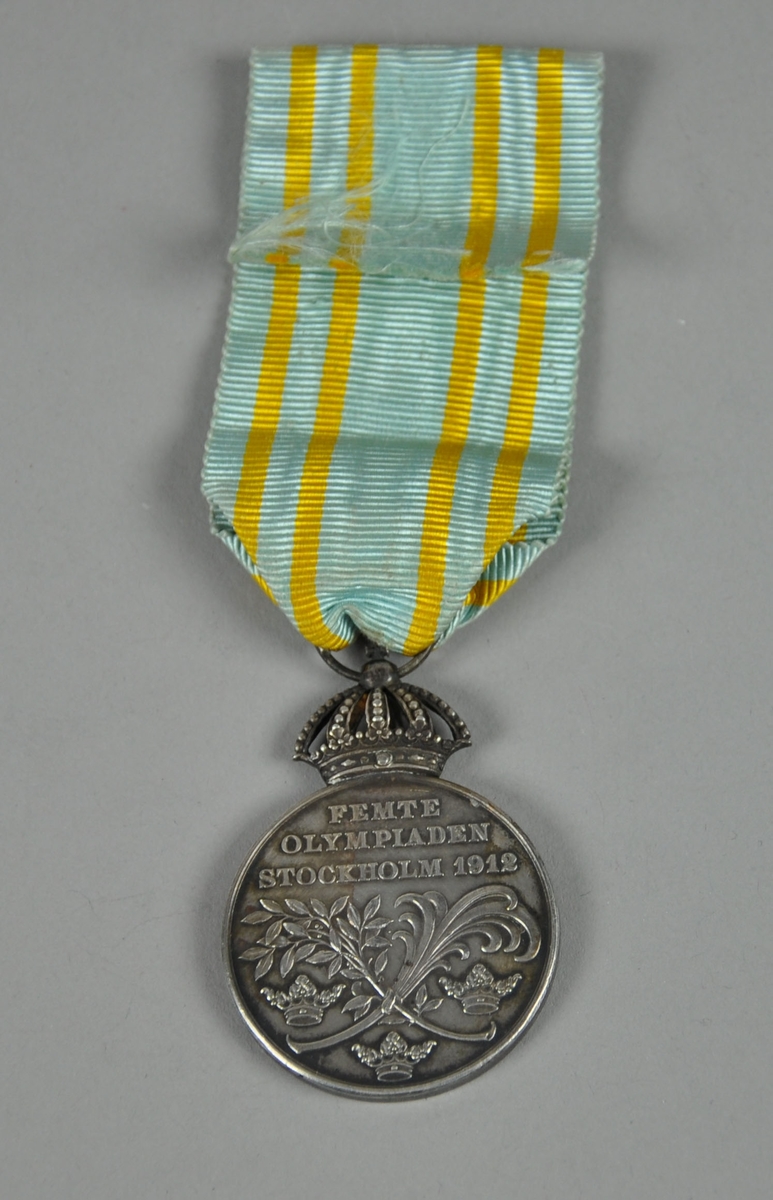 Sølvfarget minnemedalje med motiv av Kong Gustaf V i profil på den ene siden og tre kroner på den andre siden. Det er festet et opphengsbånd til medaljen. Med medaljen følger det en blå eske..