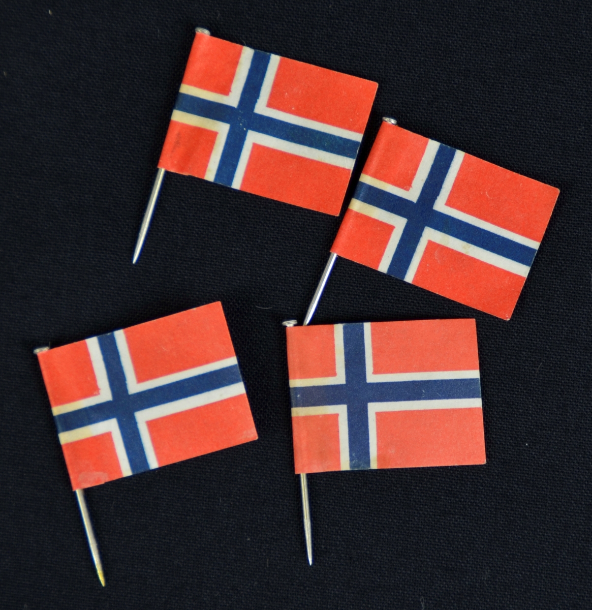 4 små, norske flagg i papir festa på knappenålar. I raudt, kvitt og blått.