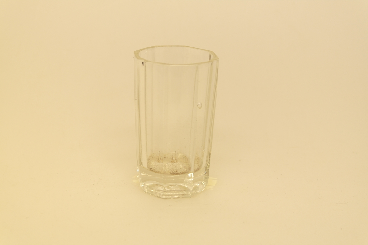 Kryddersett bestående av stativ (a), to flasker (b, c, f) og to glass (d-e).
A) Krydderstativ av tre og støpt messing. Messingkant rundt 4 sirkelåpninger. Fire balusterformede messingbein.
B) Flaske i støpt glass med glasspropp (F)
C) Flaske i støpt glass
D) Støpt glass