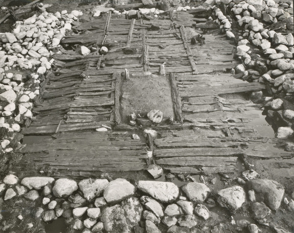 Dokumentasjonsbilder i serie fra arkeologiske utgravingar av Borgundkaupangen. De forskjellige motiva viser ei årestove, brønn og ein kavleveg ved sida av ei rekke med påler.