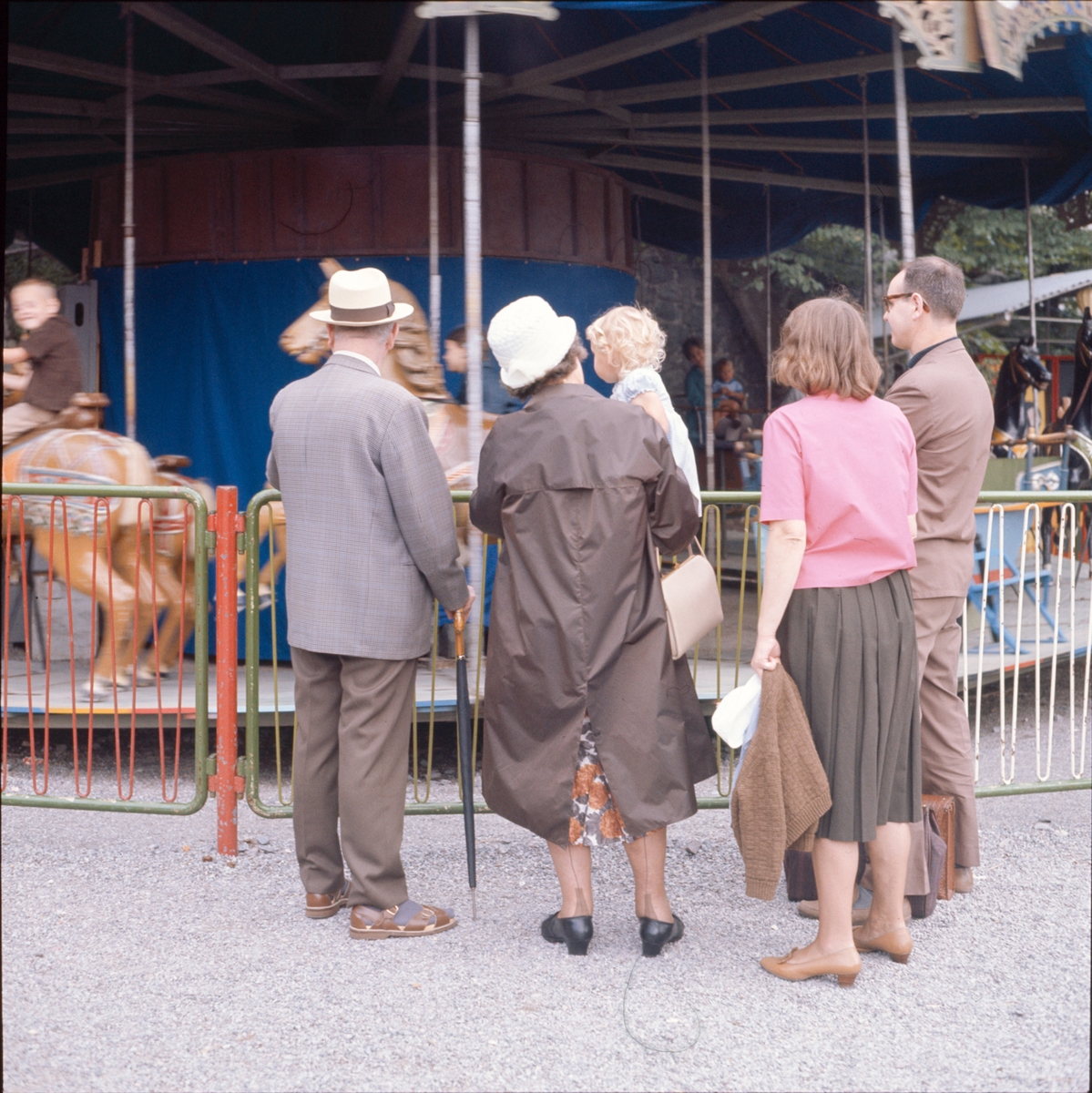 En grupp personer betraktar barn som åker karusell.