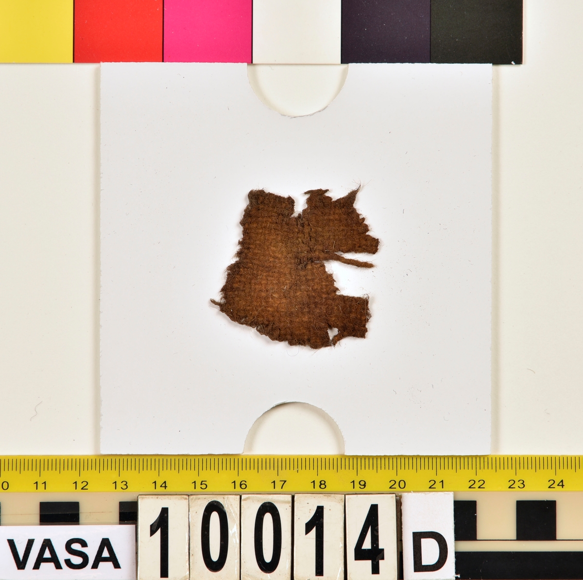 Textil.
6 textilfragment uppdelade på fyndnummer 10014a-d.
Fnr 10014a består av två fragment av ull vävd i 2/2-kypert.
Fnr 10014b består av ett fragment av ull vävd i 2/1-kypert.
Fnr 10014c består av två fragment av ull (eller bäver?) vävd i tuskaft. 
Fnr 10014d består av ett fragment av ull vävd i tuskaft.