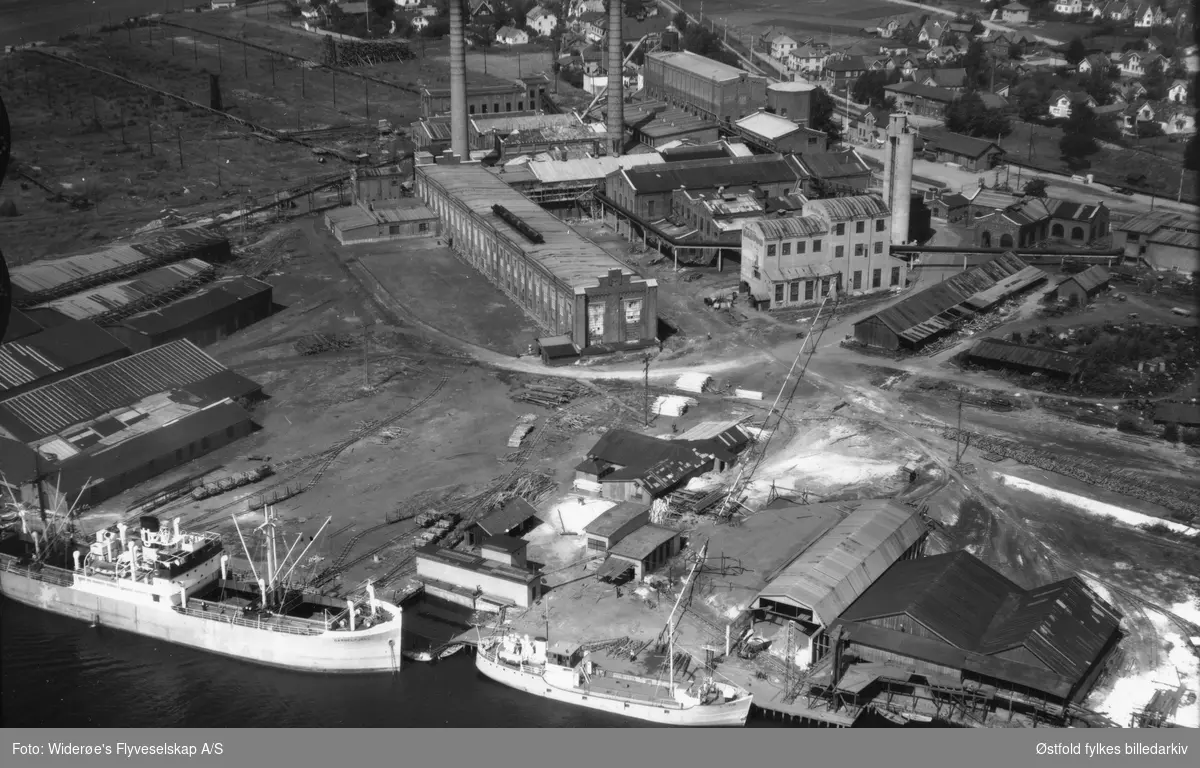Greåker Cellulosefabrikk i Tune med Glomma.    
To båter ligger til kai, til venstre Gammelfjell. Båten til høyre er Klor.
Greåker stasjon skimtes.
