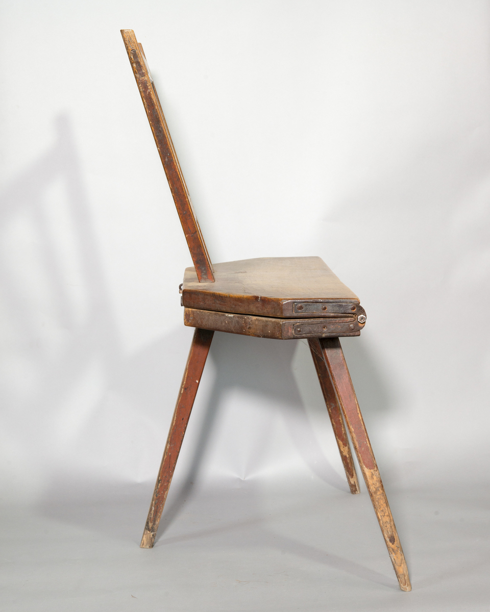Bordsstol av trä, fällbar. 8-kantig sits i nedfällt läge. Rygg med tvärband och spjälor. Tre intappade ben och ryggen fungerar som fjärde ben i nedfällt läge. Gångjärn av järn. Rester av rödbrun och gul färg.