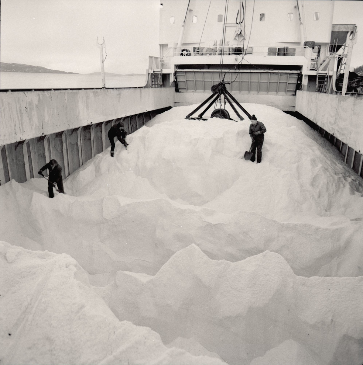 Arbeidere måker salt i et fartøy ved kaia til Kristian Holsts saltlager.